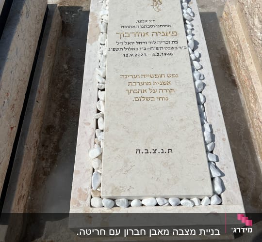 מצבה עם כיתוב בעברית ואבנים לבנות מסביב
